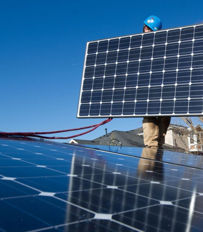 Technician installing a commercial solar panel against a blue sky